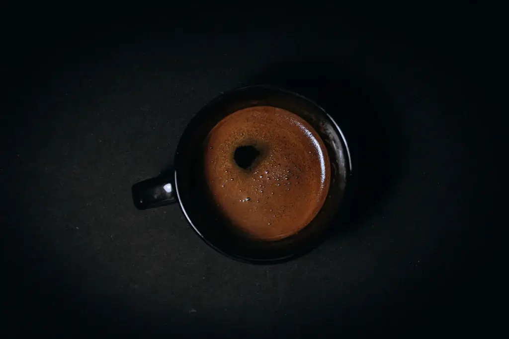 暗い背景に置いた、黒いカップのコーヒーを上から見た写真