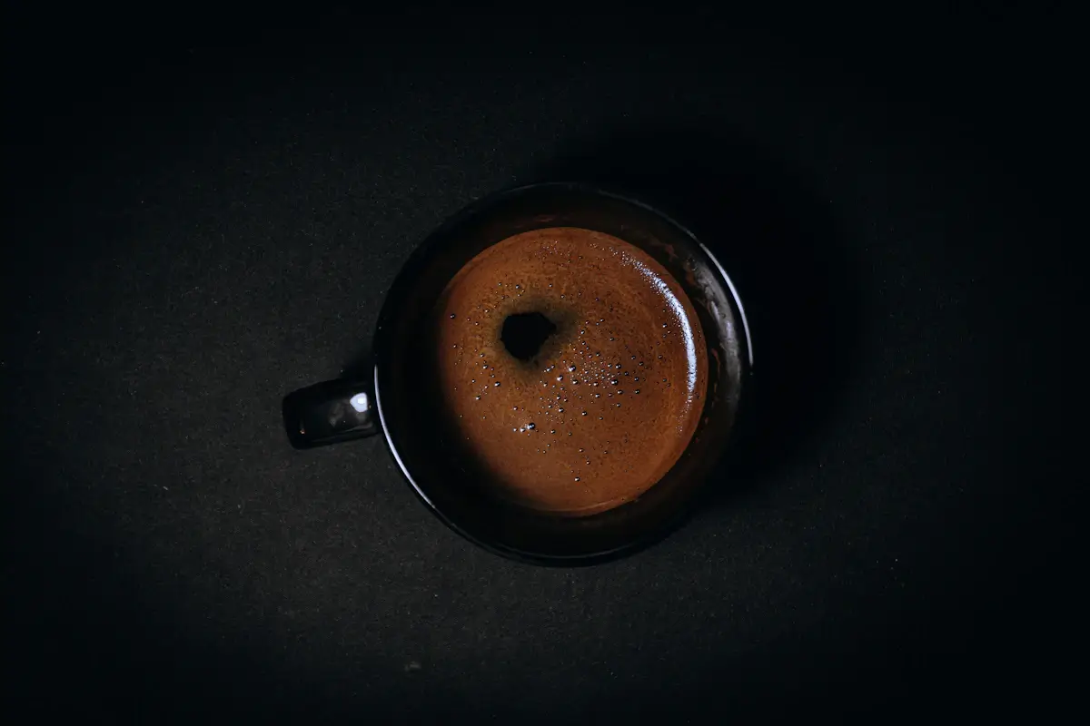 暗い背景に置いた、黒いカップのコーヒーを上から見た写真