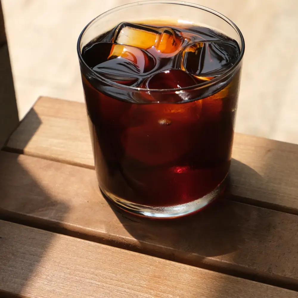木のベンチに置いた、氷の入ったグラスのアイスコーヒー