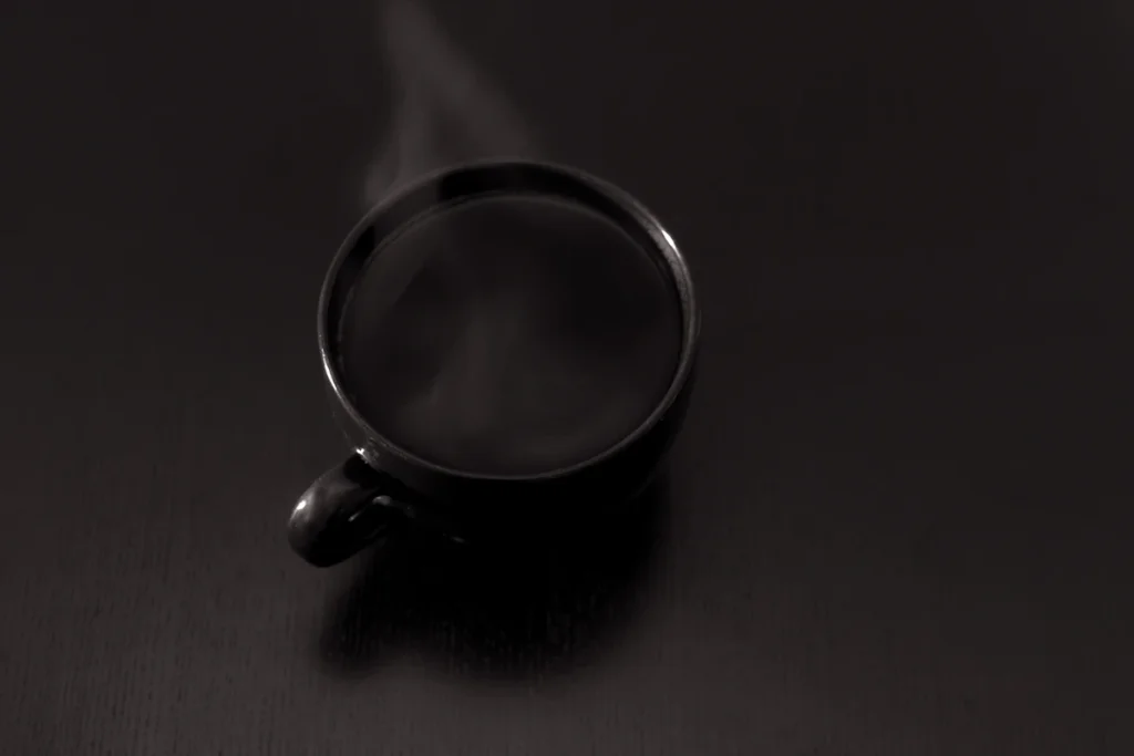 暗い場所で湯気を立てる、黒いカップのコーヒー