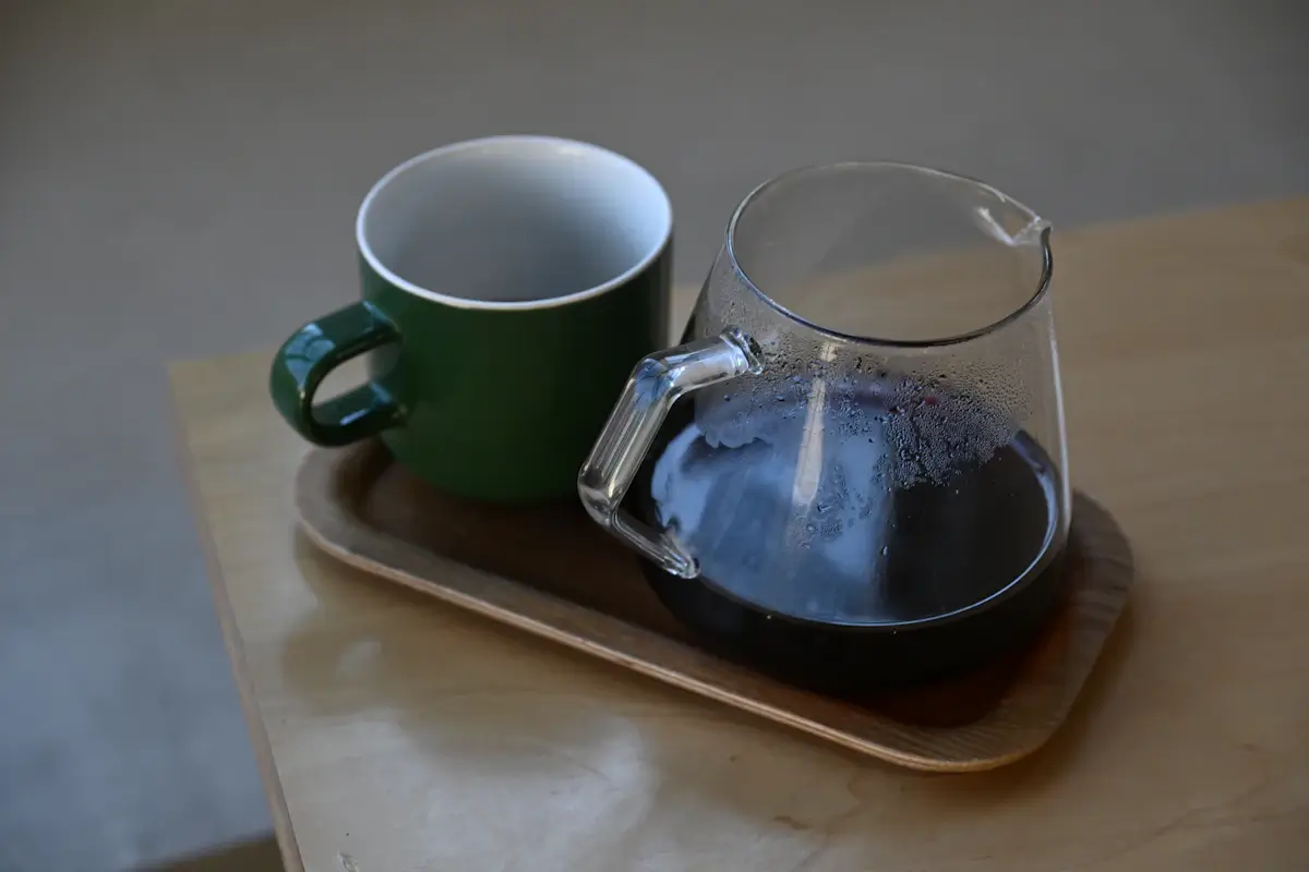 木のトレイにのせた、緑のマグカップと、コーヒーの入ったガラスのポット
