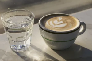 大理石のテーブルに並べた、水の入ったグラスと、ラテアートを描いたコーヒーのカップ。横から日が差している