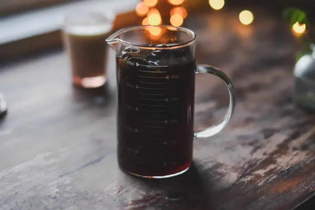木のテーブルに置いた、目盛りつきのガラスのピッチャーに入ったコーヒー