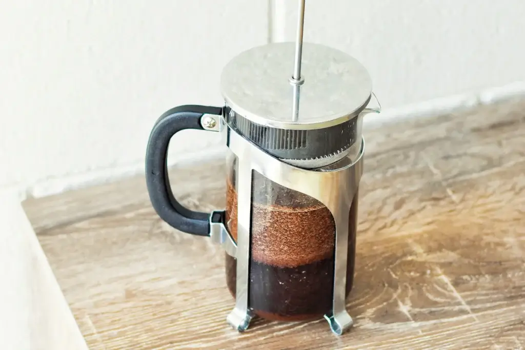 木のテーブルに置いた、コーヒーの入ったフレンチプレス