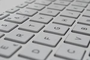 白いキーボードのキーを、斜めから近くで写した写真。キーにはアルファベットや数字が印字されている