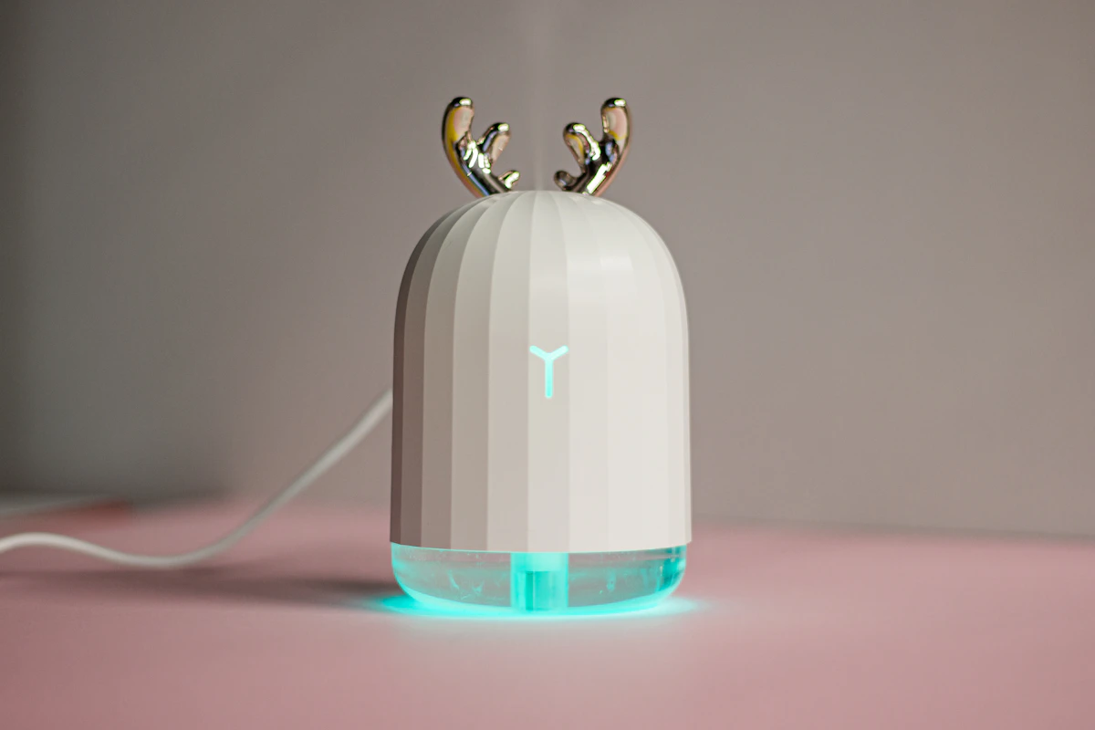 ピンク色の台の上に置いた、白い小型の加湿器。上に金色の角の飾りが付き、下の部分が水色に光っている
